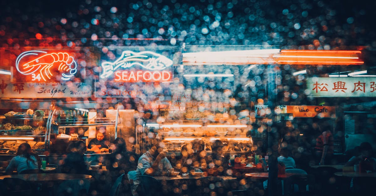 Explore the neon-lit ambiance of a bustling seafood market in Kuching at night, captured through a rain-splattered lens.