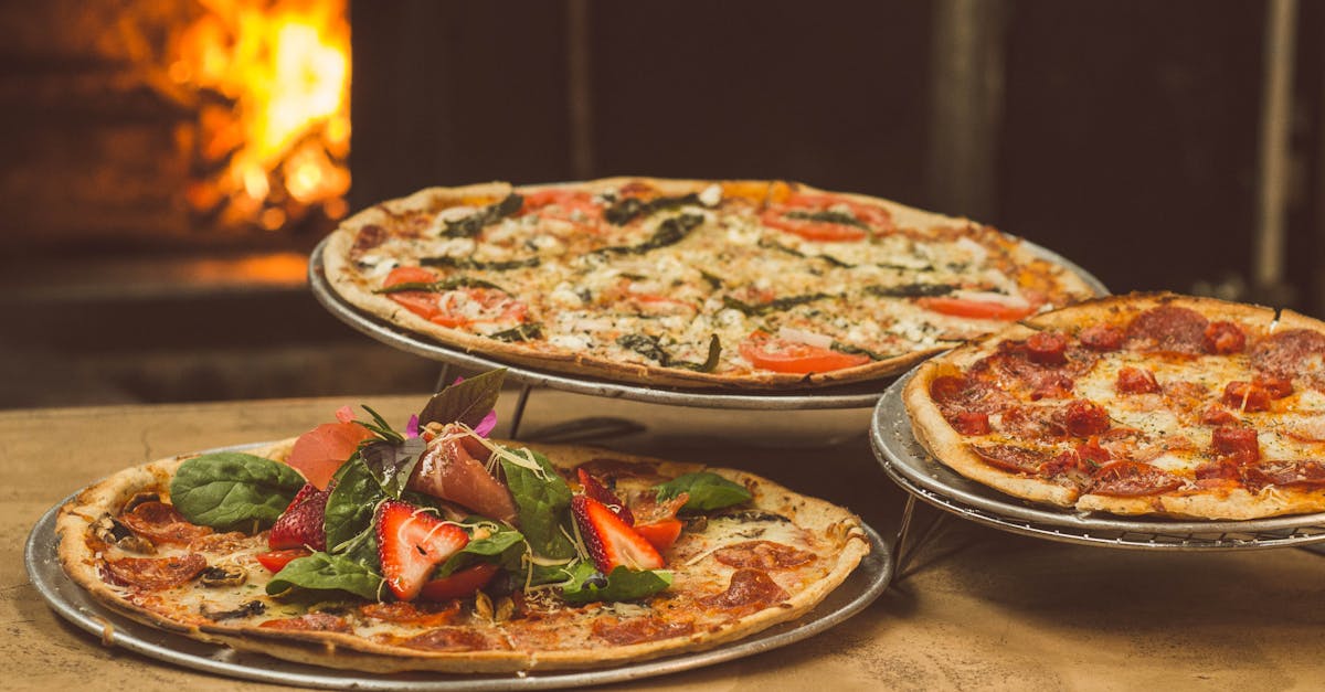 Trio of gourmet pizzas with unique toppings near a wood-fired oven, ideal for food enthusiasts.