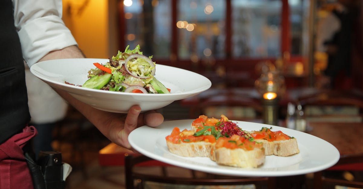 A waiter serves a fresh salad and hors d'oeuvres in a cozy restaurant setting.